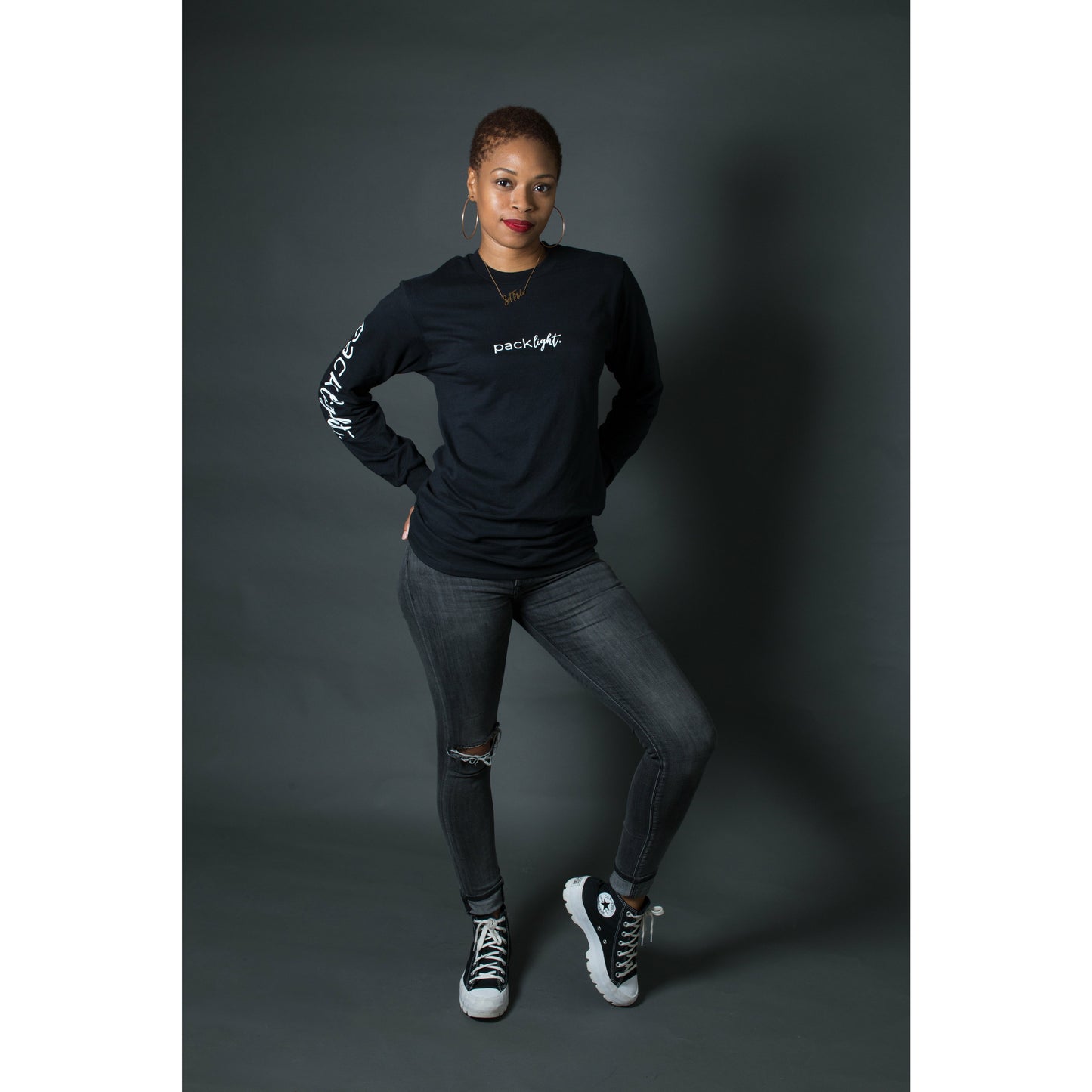 woman model wearing black affirmation tee that says Pack Light on the sleeve and front of the tee by Sol Rise Essentials