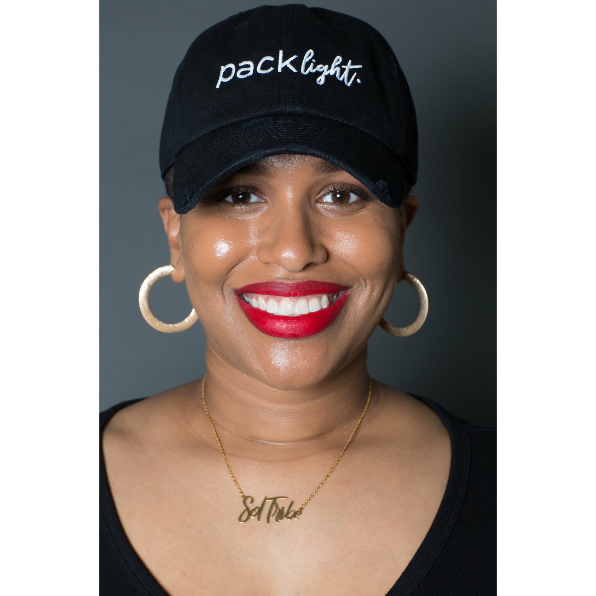 smiling woman model wearing black Pack Light affirmation hat from Sol Rise Essentials