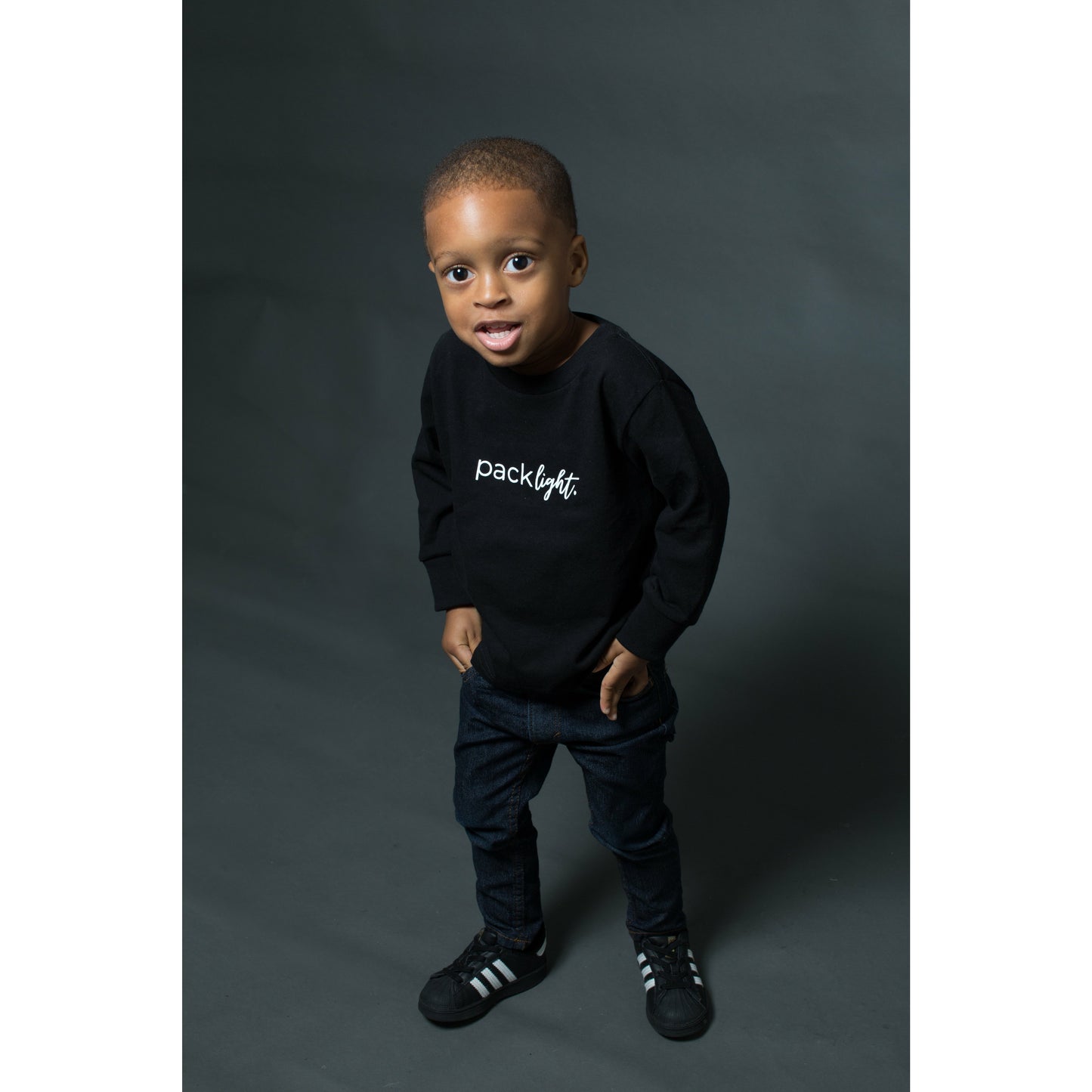 boy model wearing black long sleeve affirmation tee that says Pack Light by Sol Rise Essentials 