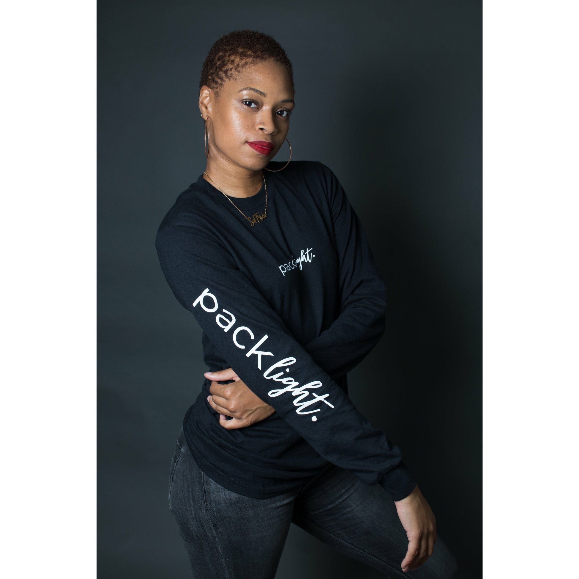 woman model wearing black affirmation tee that says Pack Light on the sleeve and front of the tee by Sol Rise Essentials